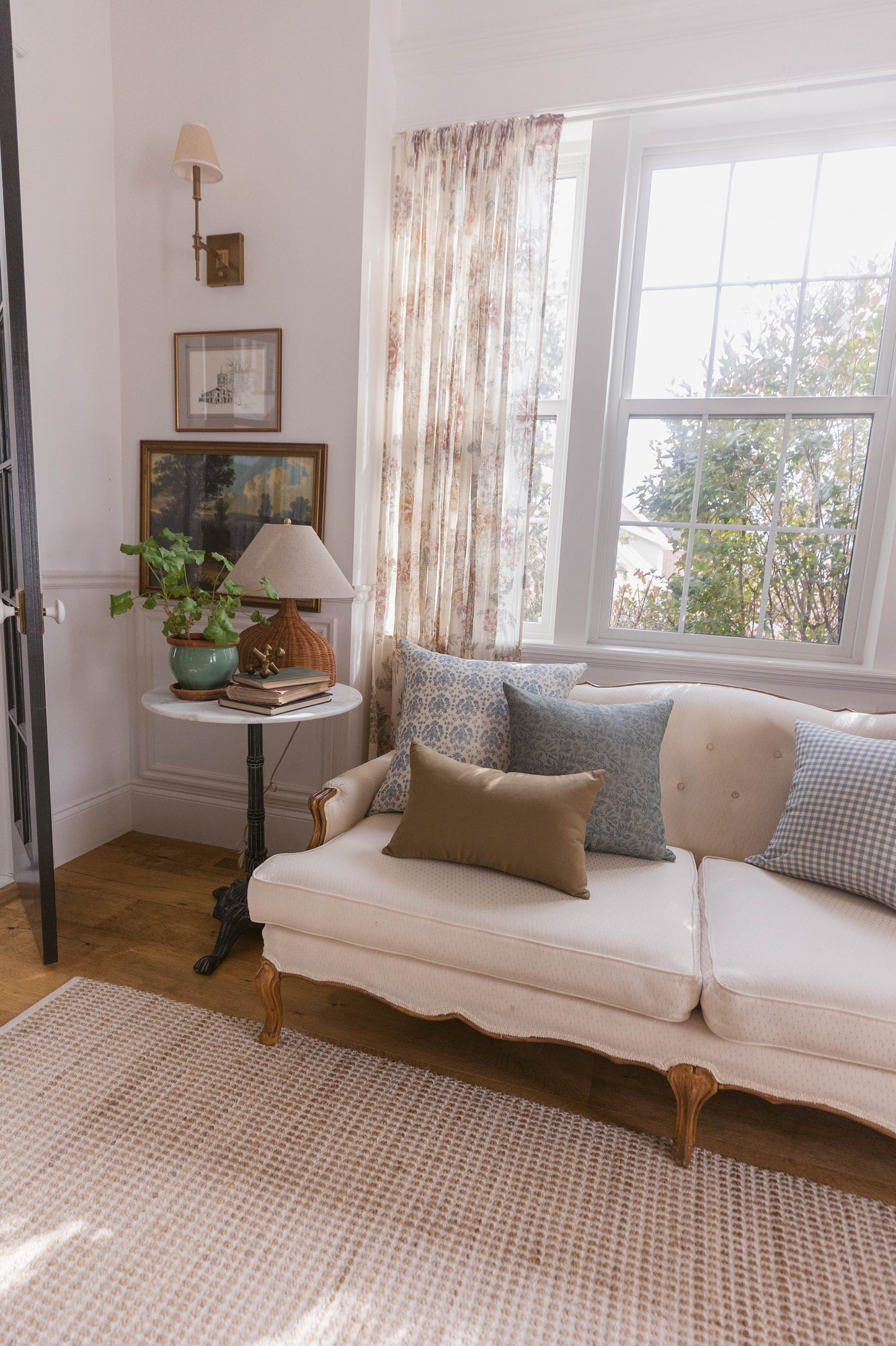 Cream upholstered sofa with decorative pillows in a living room with pink walls and large windows.