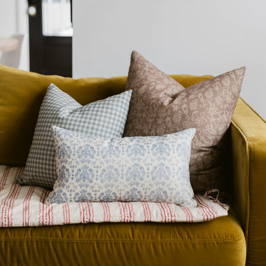 Blue and white damask patterned lumbar pillow displayed on a mustard yellow sofa with coordinating decorative pillows.