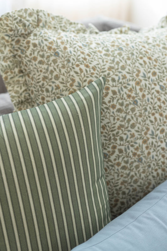 Green and cream striped pillow in foreground with floral patterned pillows behind it on bed.