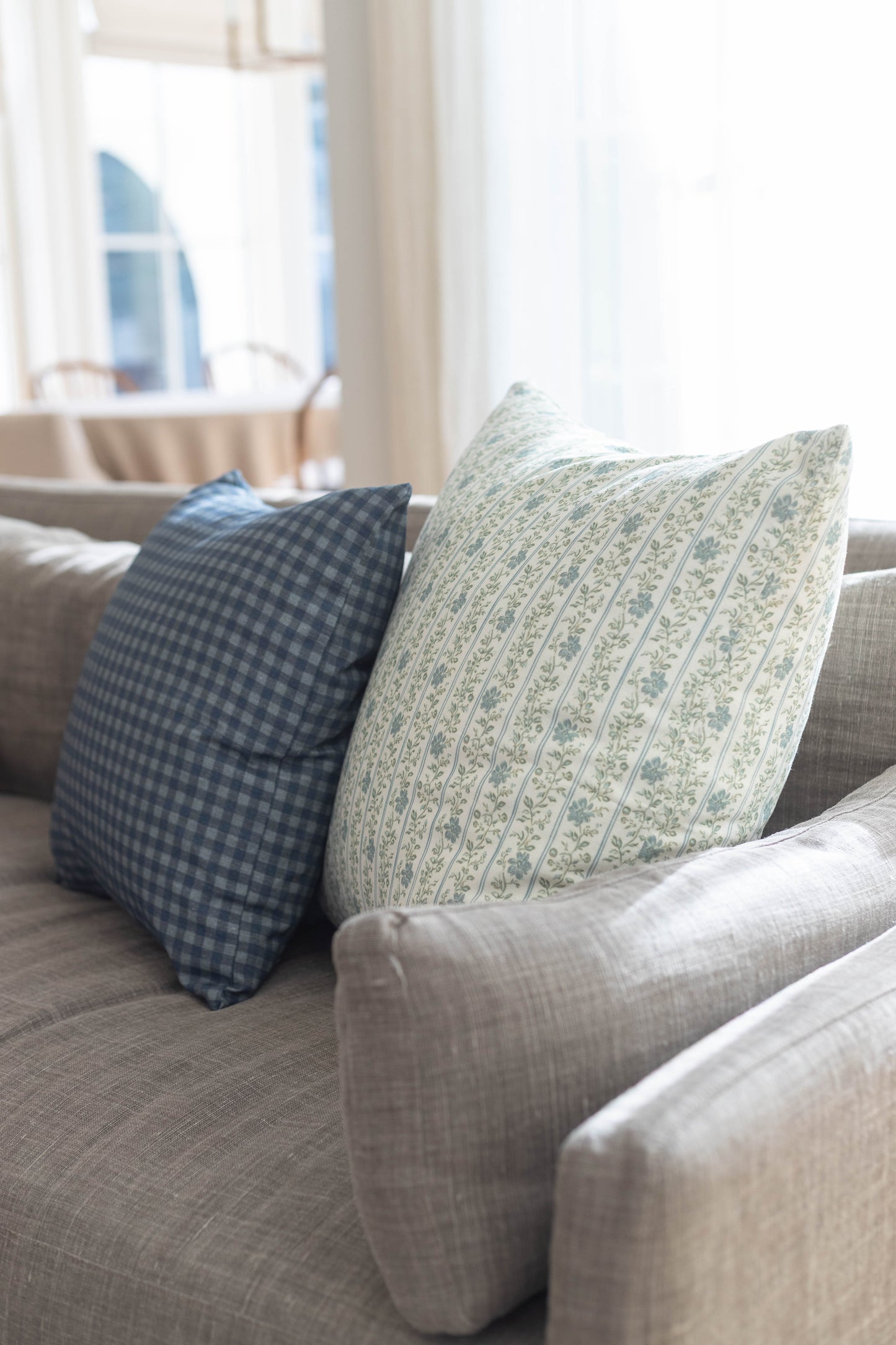 Light blue gingham and cream floral striped decorative pillows on a gray upholstered sofa.