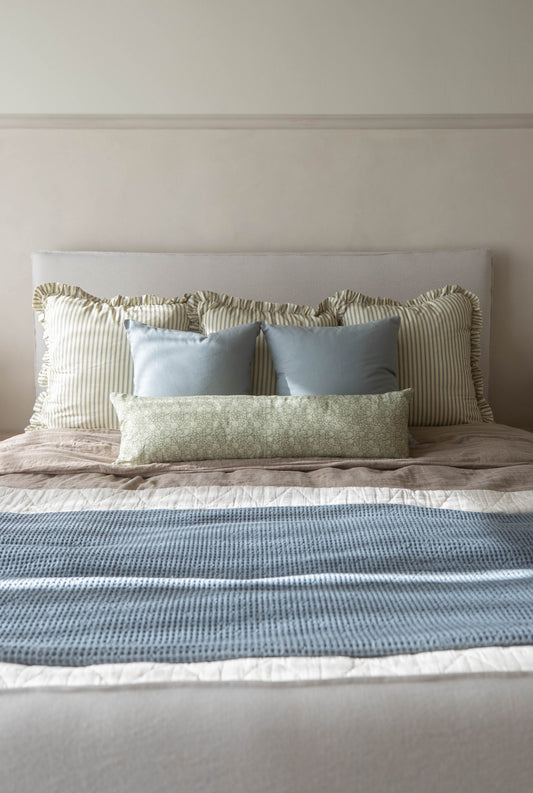 Striped Ellis Ruffle pillow with ruffled edges displayed on bed among blue and green patterned pillows.
