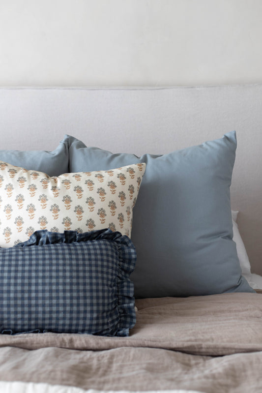 Three decorative pillows arranged on a bed: a floral patterned pillow, a blue-gray solid pillow, and a navy gingham pillow wi