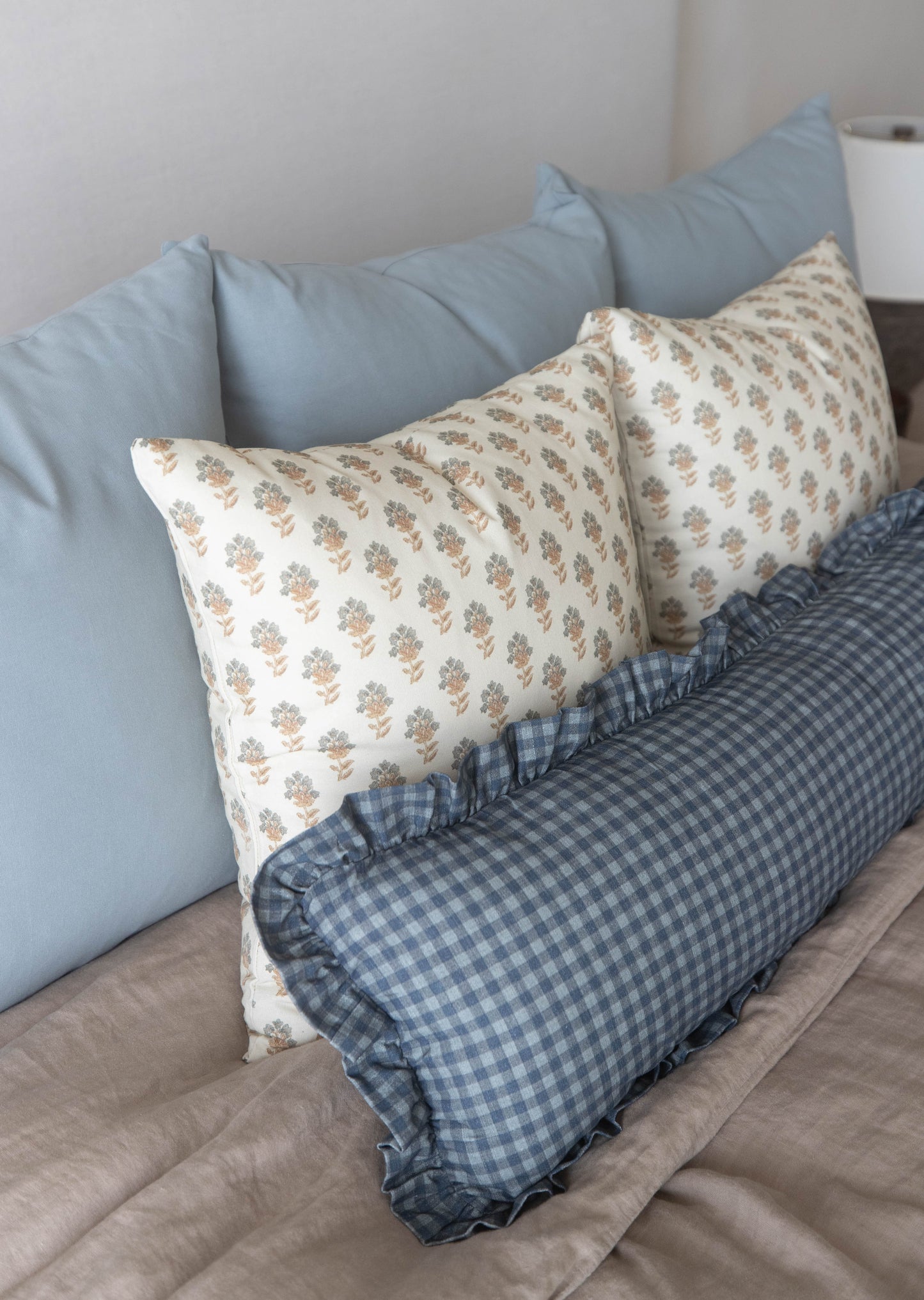 Decorative pillows with floral and checkered patterns arranged on a bed with blue and gray solid pillows.