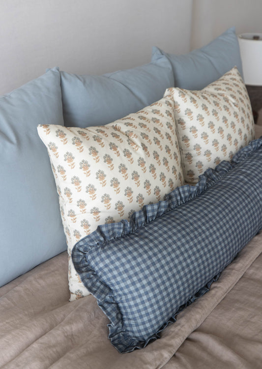 Decorative pillows with floral and checkered patterns arranged on a bed with blue and gray solid pillows.
