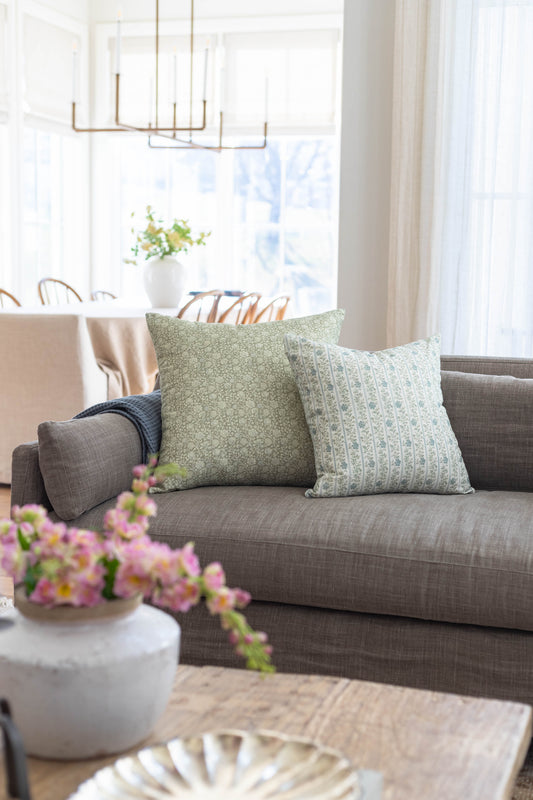 Two decorative pillows with green floral and striped patterns on a gray upholstered sofa.
