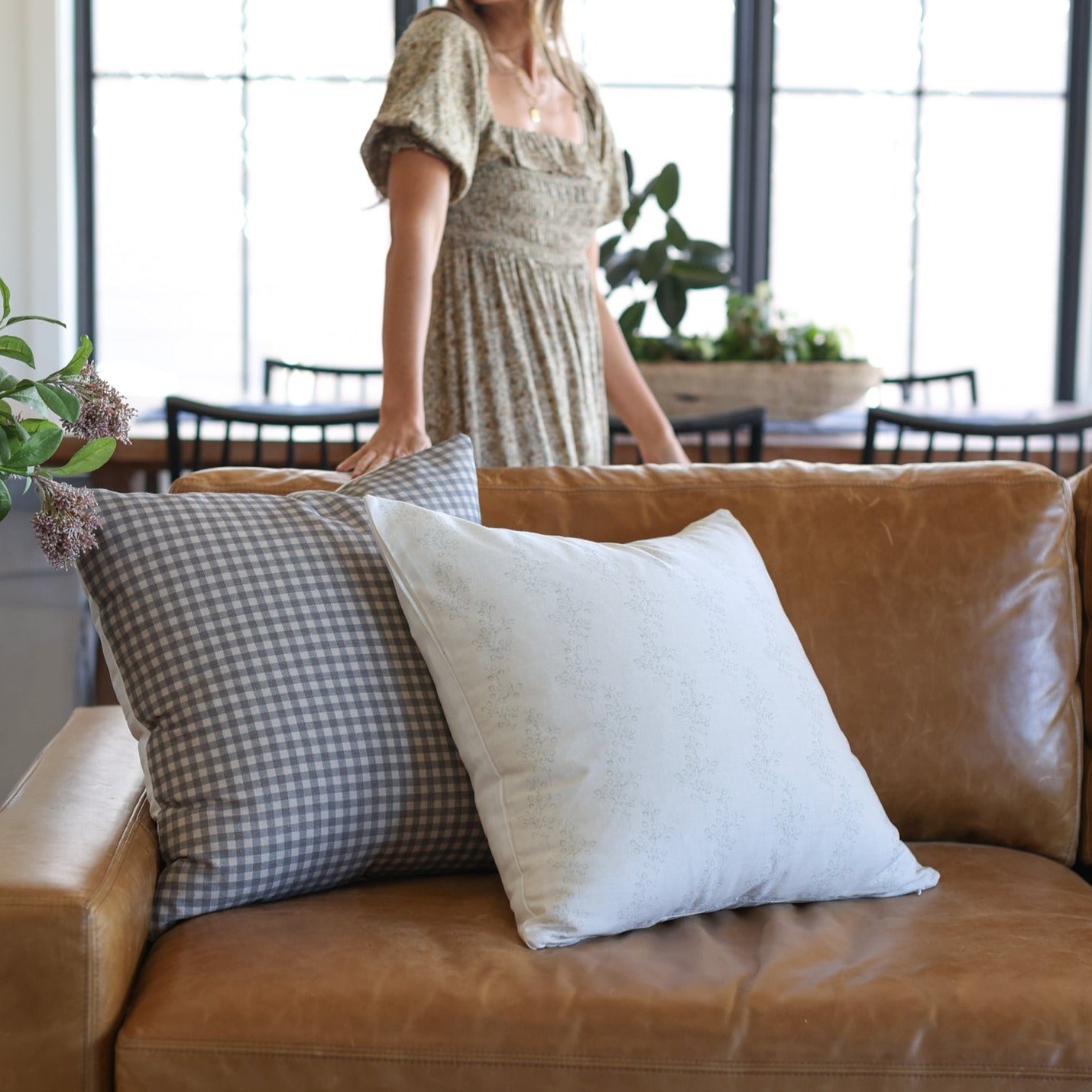 Gray gingham and white textured throw pillows arranged on a tan leather sofa.