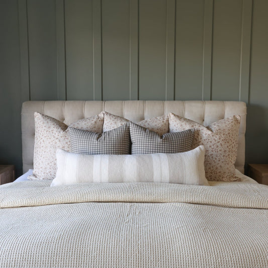 Brown and white gingham checkered pillows arranged on a bed with cream headboard and coordinating bedding.