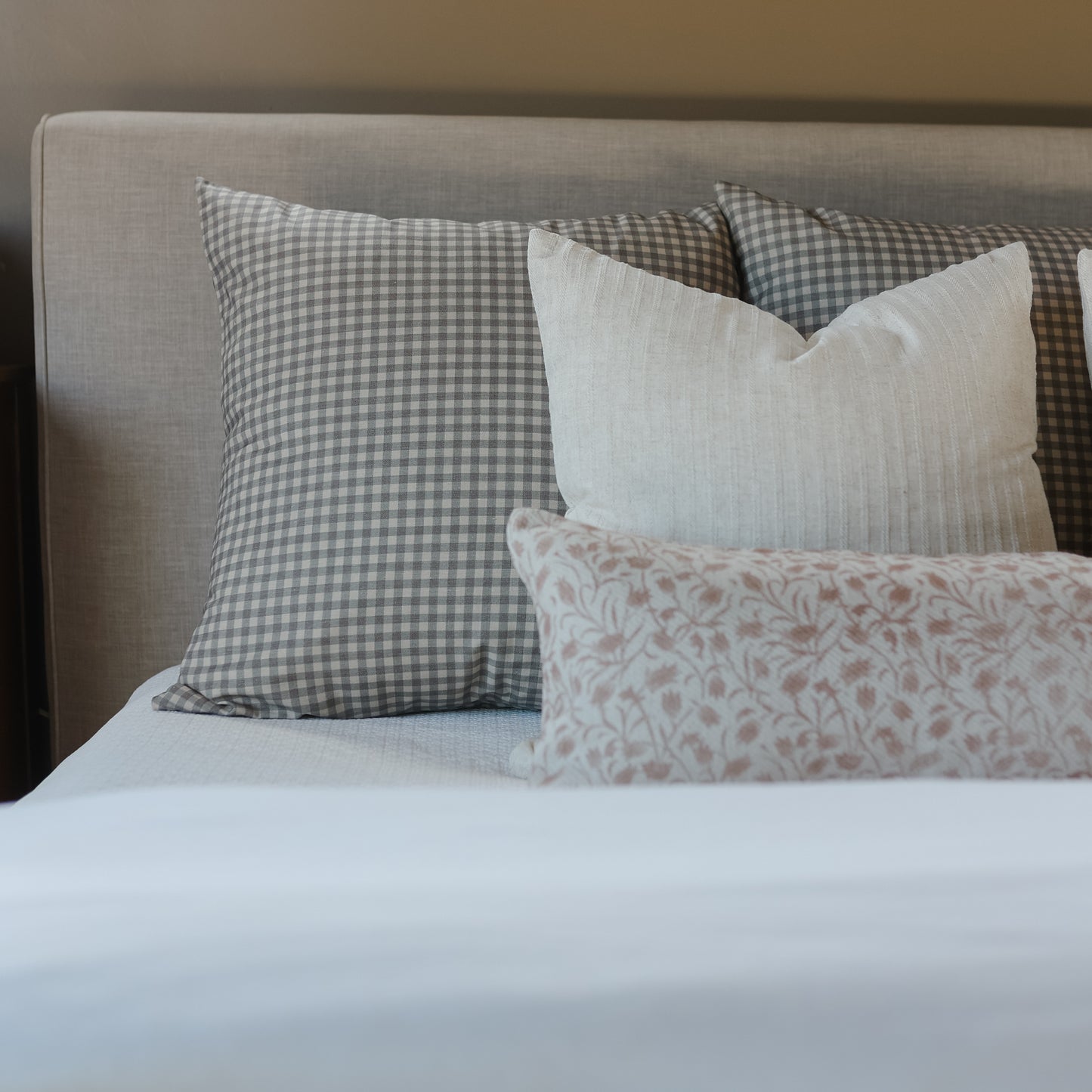 Brown and white gingham check pillow displayed on bed with coordinating pillows and white linens.
