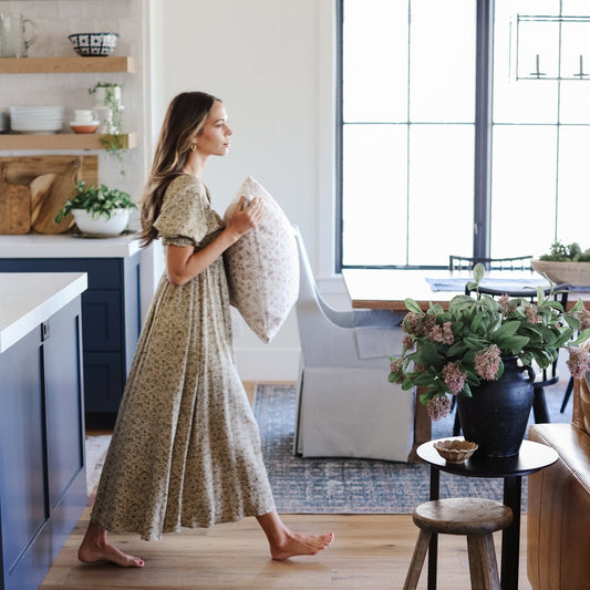 Woman holding a cream and gray patterned throw pillow in a modern kitchen and living room setting.
