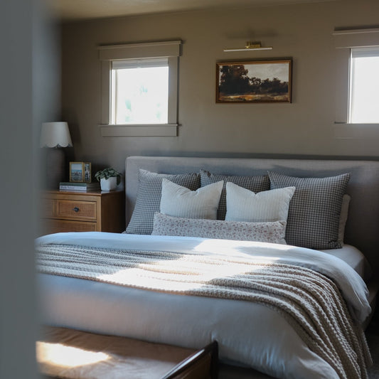Brown and white gingham patterned pillows and throw blanket arranged on a bed with white and gray bedding.