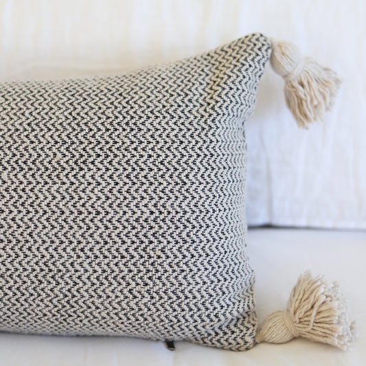 Cream and charcoal tweed lumbar pillow with tassel corners and woven texture pattern.