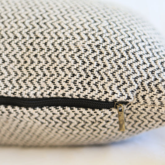 Cream and charcoal tweed pillow with black zipper and brass pull detail.
