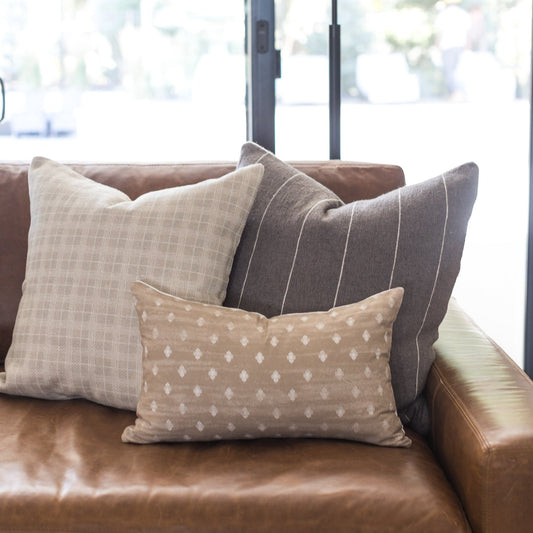 Taupe throw pillow with white geometric diamond pattern on brown leather sofa.