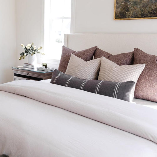 Charcoal lumbar pillow with white stripes displayed on a bed with coordinating patterned pillows.