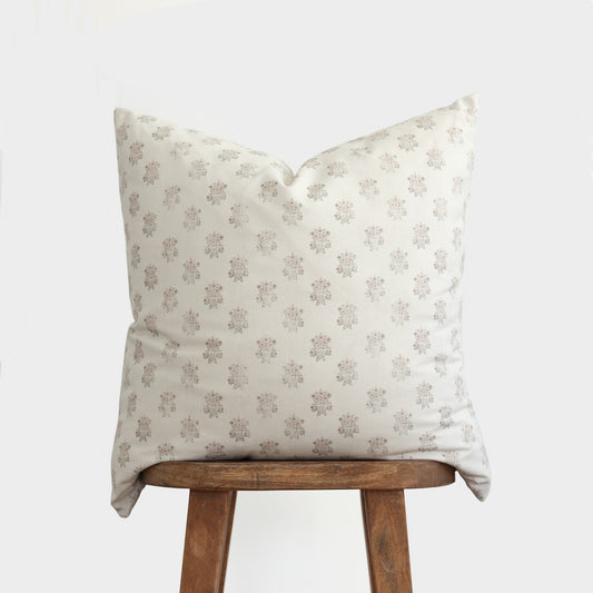 Cream pillow with mauve floral pattern displayed on wooden stool.