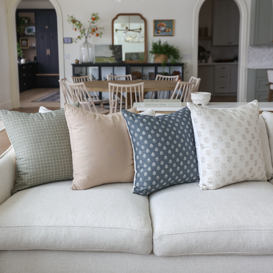 Four tan and blue patterned throw pillows arranged on a beige sofa in a living room setting.
