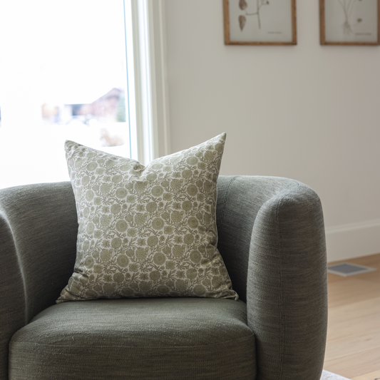Green and cream patterned square pillow displayed on a gray upholstered armchair.