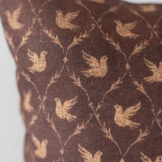 Brown cushion with tan dove silhouettes in a geometric lattice pattern.