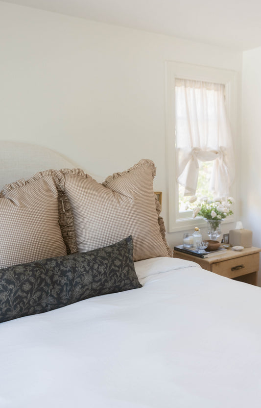 Tan and white mini gingham pillows with ruffled edges arranged on a bed.