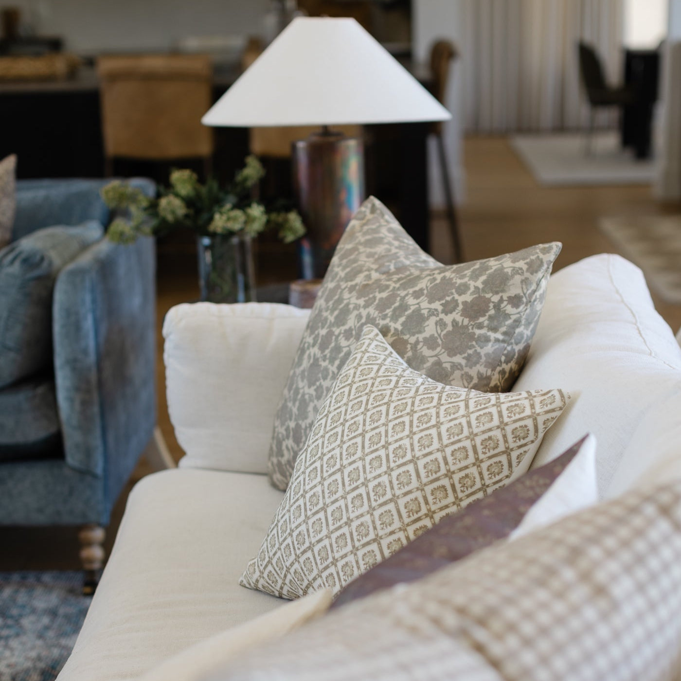 Two patterned linen pillows in taupe and cream geometric designs arranged on a white upholstered chair.