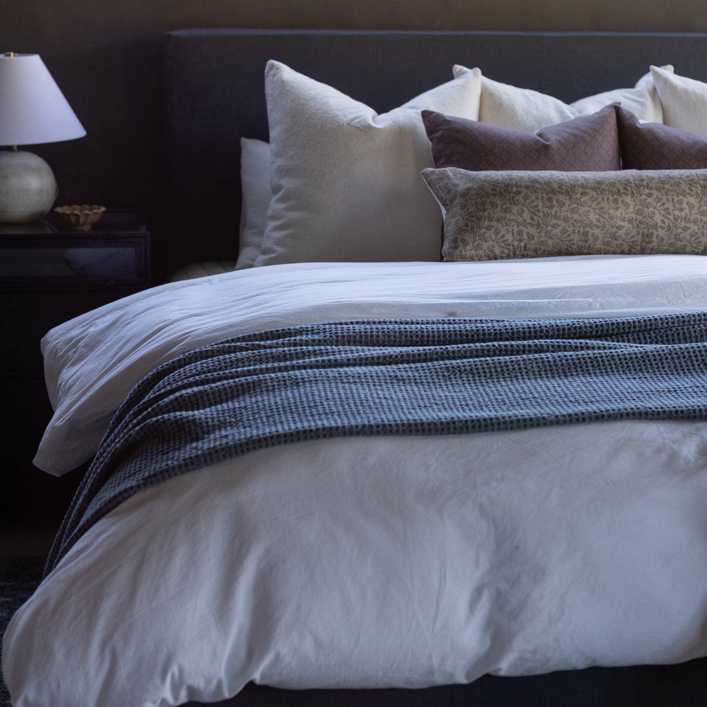 Faye pillow displayed on a bed with white bedding, navy striped throw, and coordinating cream and gray decorative pillows.