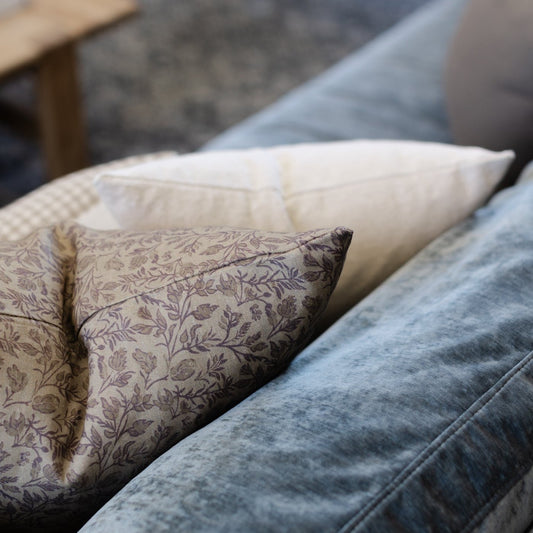 Decorative pillows in taupe floral, cream textured, and cream check patterns arranged on blue upholstered furniture.