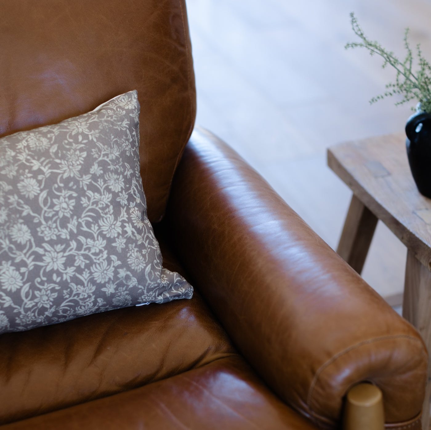 Brown leather armchair with gray and white damask patterned pillow, wooden frame detail visible.