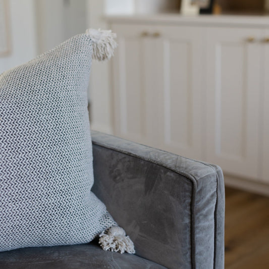 Cream tweed pillow with textured weave and fringe tassel detail on gray upholstered chair.