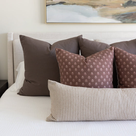 Brown and beige pillows arranged on a bed, including solid brown, patterned damask, and striped designs.
