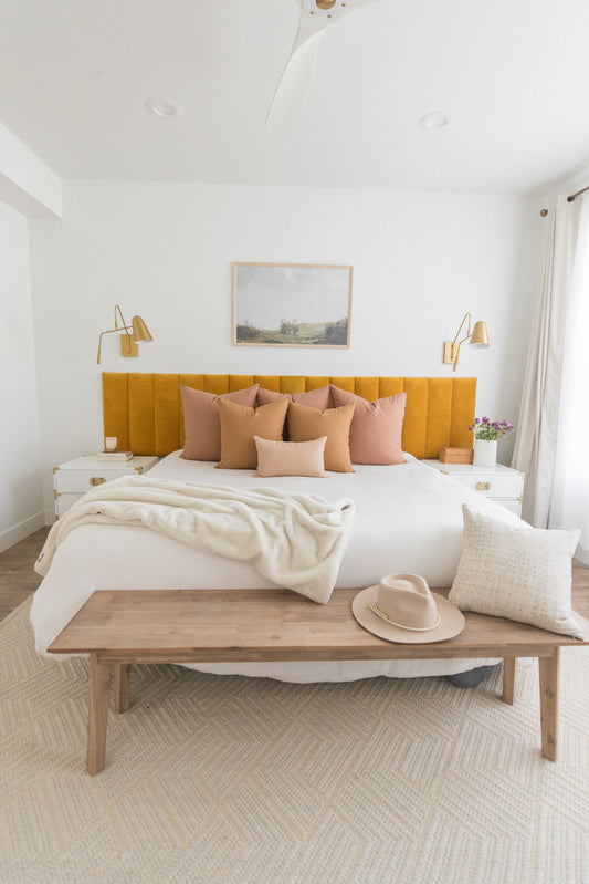 Dusty rose and tan throw pillows arranged on a bed with yellow headboard in a modern bedroom.
