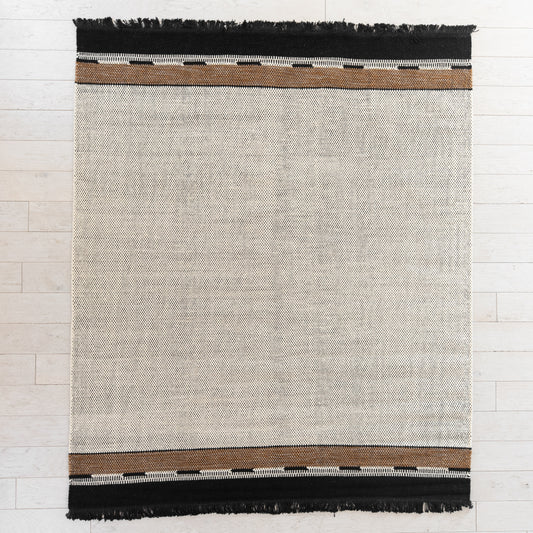 Flat-woven rug with cream center, brown and white striped borders, and black fringe on top and bottom edges.
