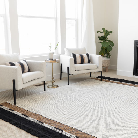 Cream upholstered armchair with black legs and striped accent pillow in modern living room setting.