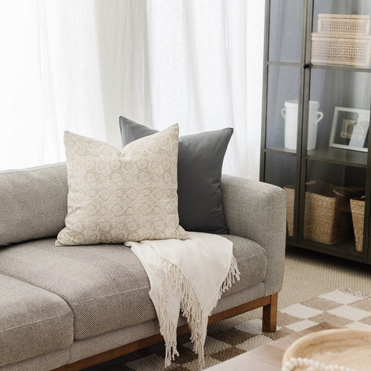 Beige patterned pillow cover and charcoal solid pillow cover displayed on a gray upholstered sofa.