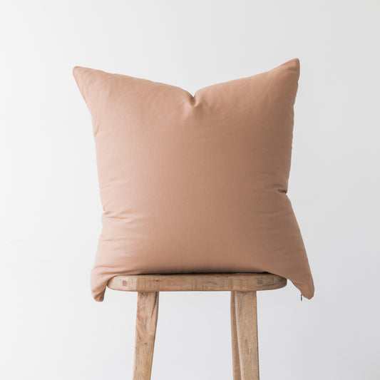 Dusty rose solid throw pillow with envelope closure displayed on wooden stool.