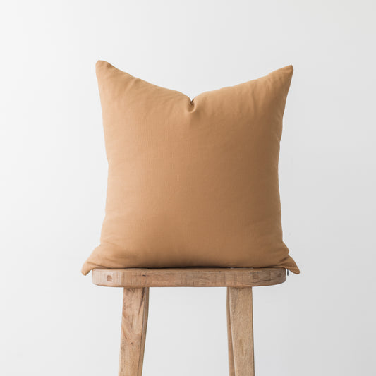 Terracotta-colored pillow with solid fabric displayed on wooden stool.