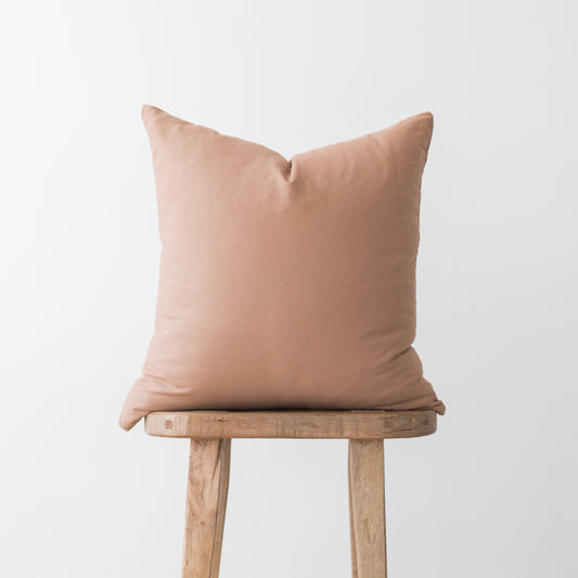 Dusty rose square pillow cover displayed on wooden stool against neutral background.