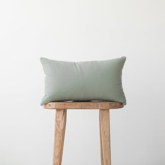 Sage green rectangular pillow with solid woven fabric displayed on wooden stool.