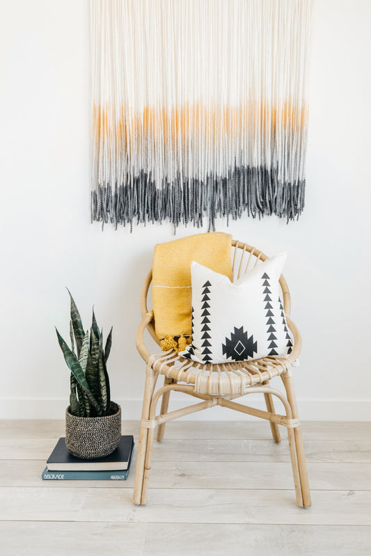 Woven wall hanging with cream, mustard, and charcoal ombre stripes displayed above a rattan chair.