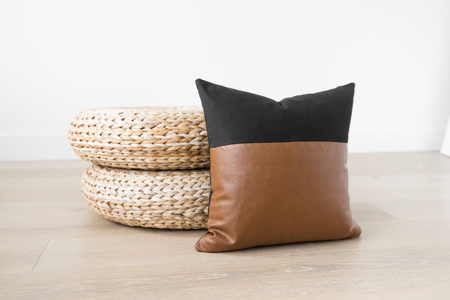 Black and tan leather pillow with pointed top next to woven natural fiber poufs.