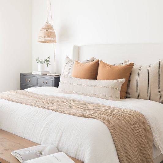 Terracotta-colored throw pillows arranged on a bed with white bedding and a tan woven throw.