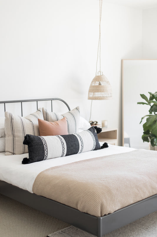 Rectangular lumbar pillow with dark gray and white horizontal stripes and black tassels on a bed.