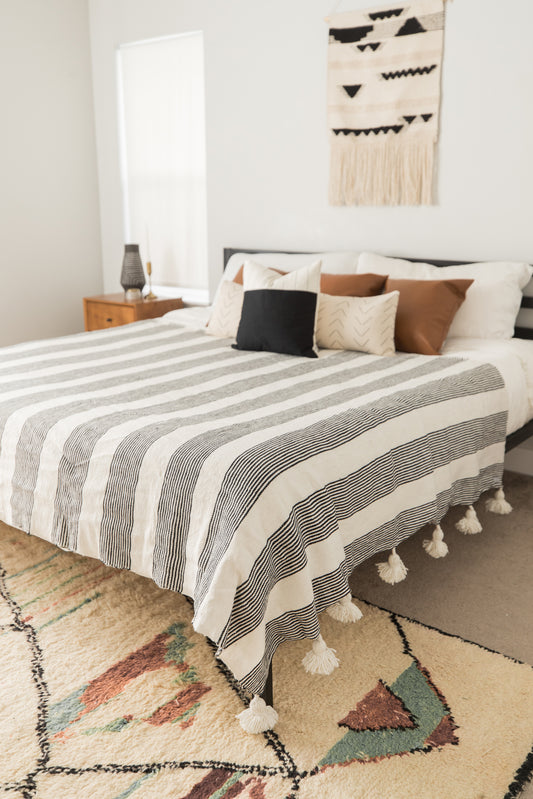 Large striped bedspread with tassel fringe in cream and charcoal gray on a king/queen bed.