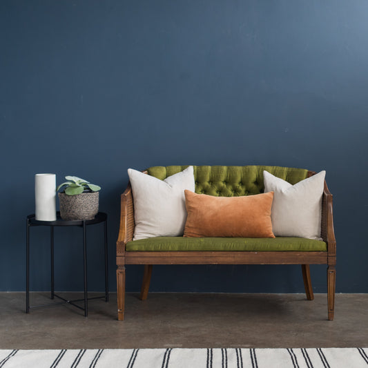 Rust velvet lumbar pillow displayed on wooden sofa with white and green cushions.