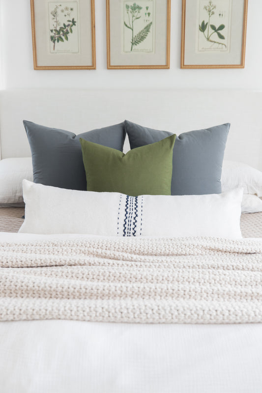 Bed styled with white lumbar pillow with navy stitching, olive and gray square pillows, and cream textured throw.