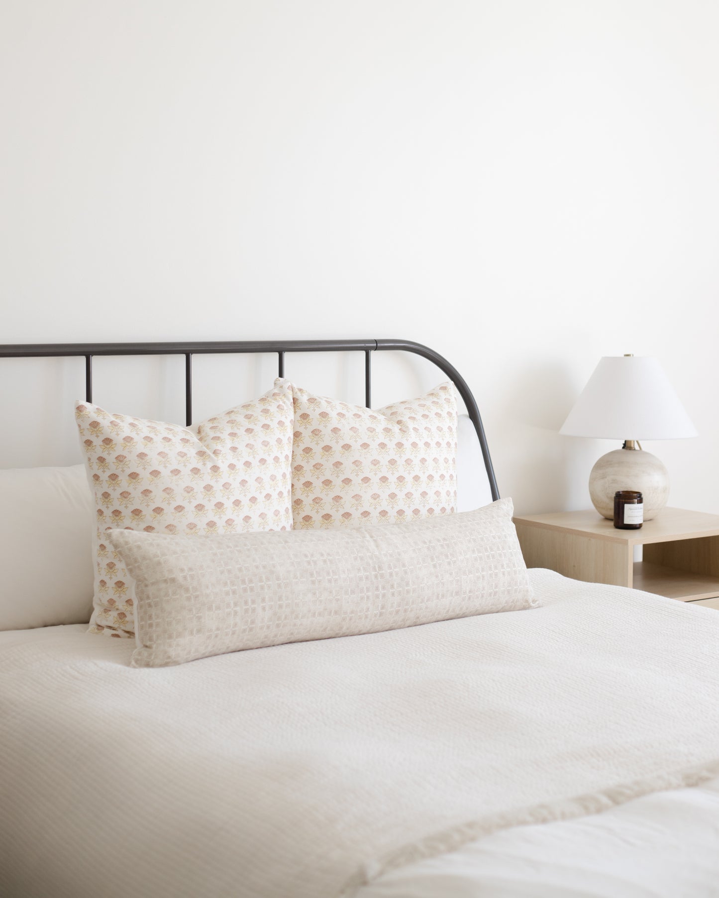 Rectangular lumbar pillow with cream grid pattern displayed on bed with matching square pillows.