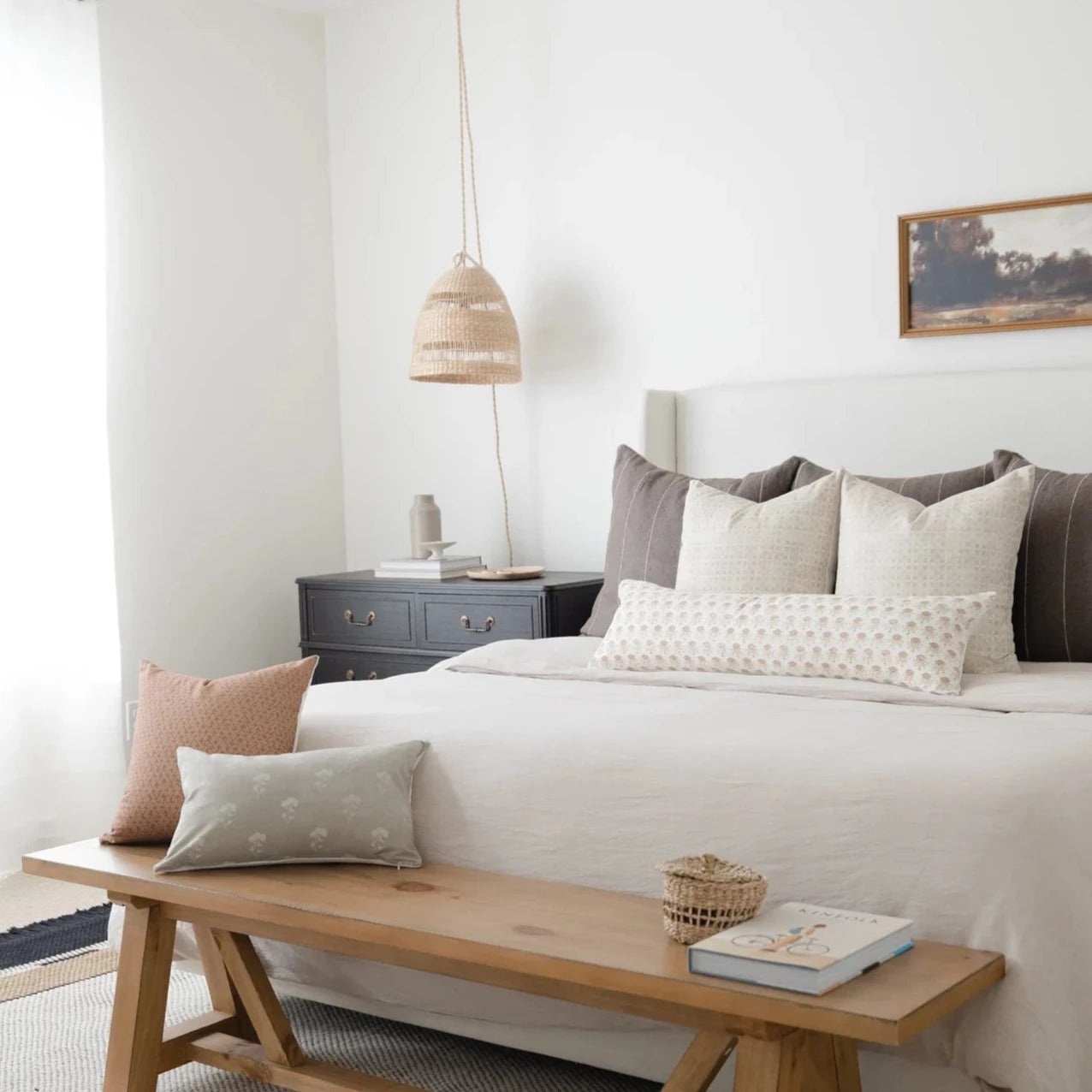 White lumbar pillow with small floral pattern displayed on wooden bench at foot of bed.