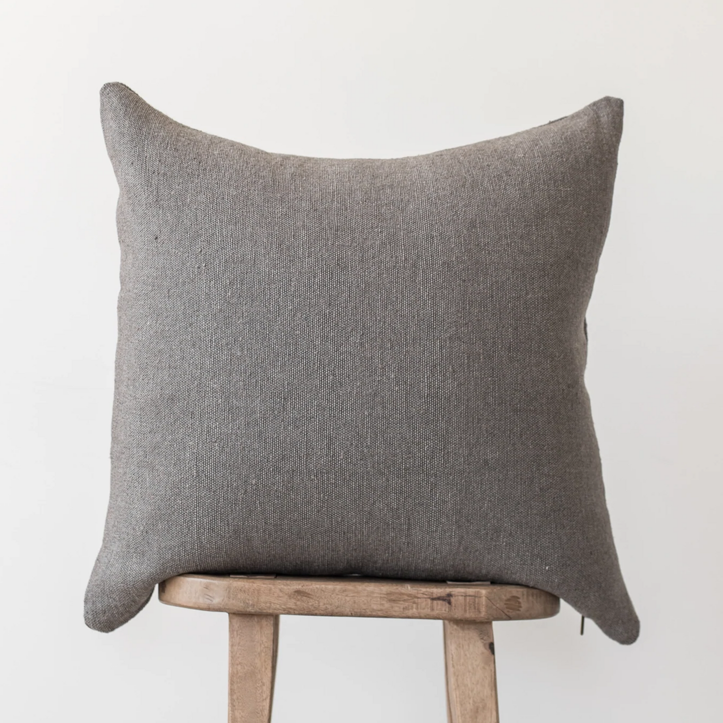 Gray woven pillow with pointed corners resting on a wooden stool.