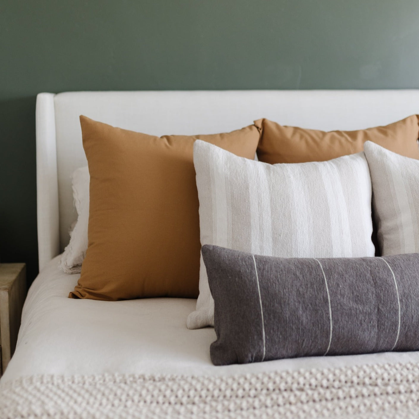 Tan solid pillow displayed on bed with white, cream, and gray striped pillows.