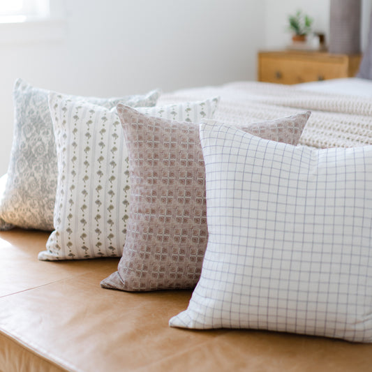 Four decorative pillows in varying neutral patterns including geometric and grid designs, arranged on a wooden floor.