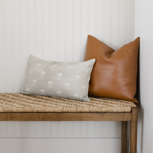 Gray lumbar pillow with white floral pattern displayed on wooden bench.